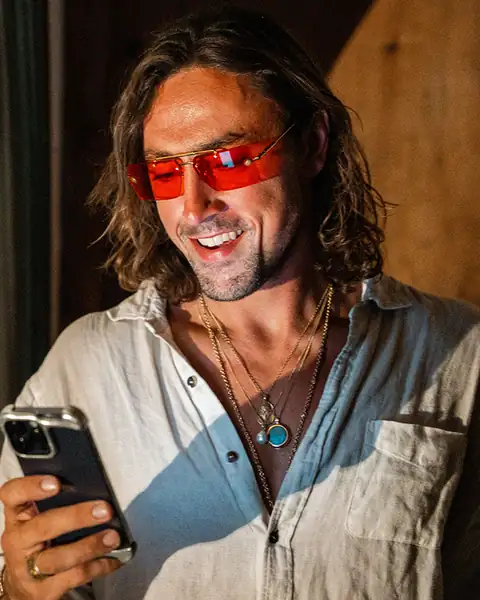 Sol Brah in Ra Optics red lenses, smiling at his phone